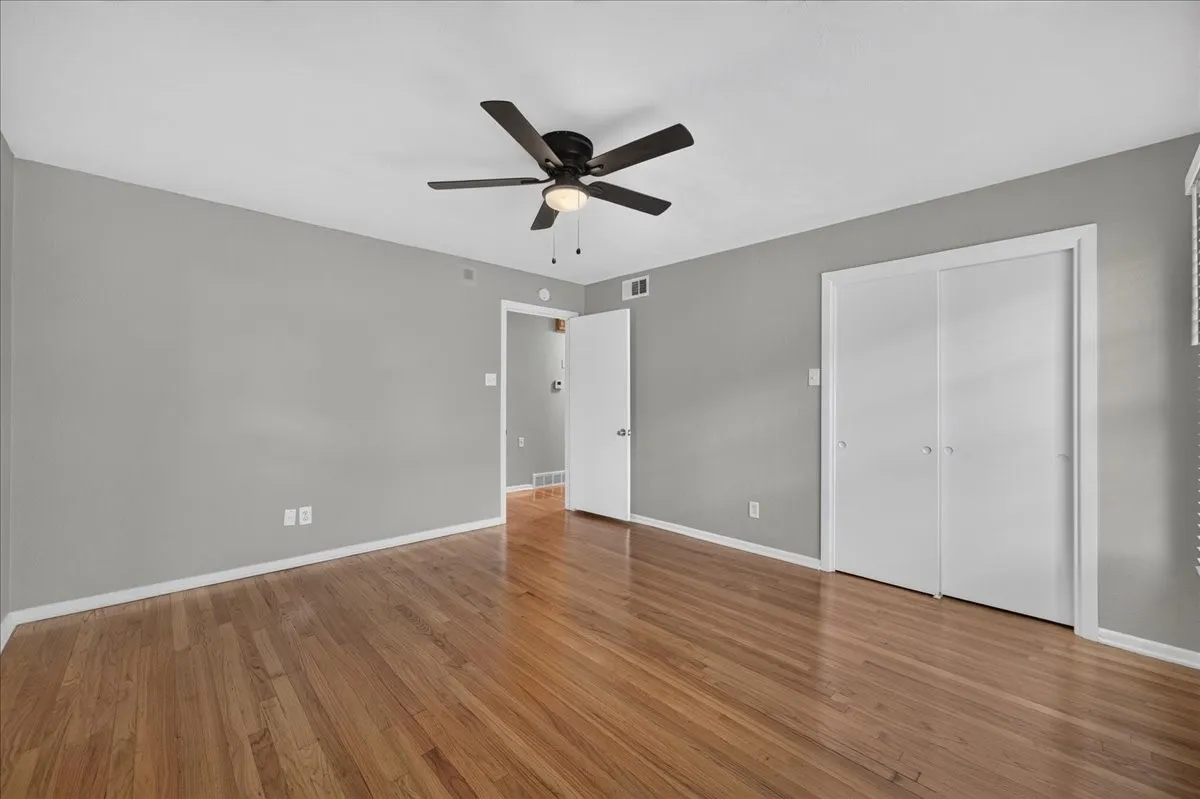 Wood-finish flooring, neutral gray walls, ceiling fan with light fixture, white trim, and white bi-fold closet doors