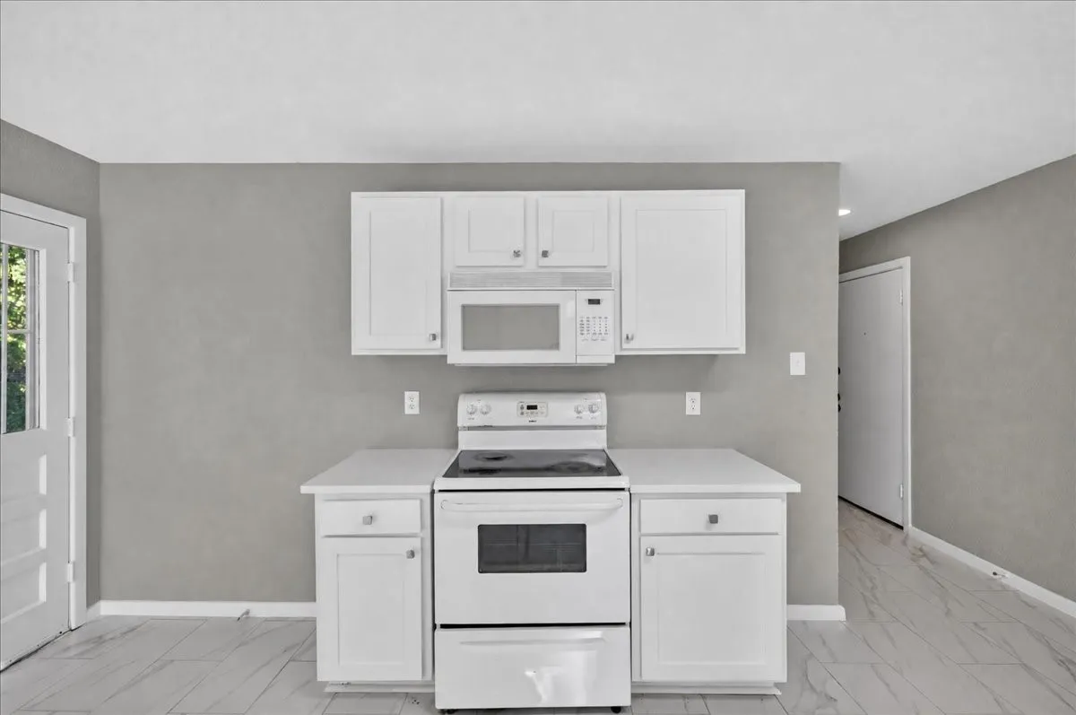 White cabinetry with silver hardware, white countertop, white range, and built-in microwave