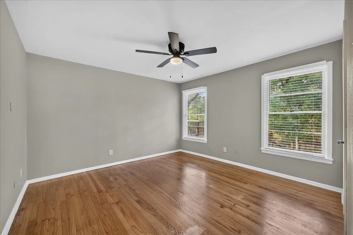 Wood-finish flooring, white trim, two windows, and a ceiling fan