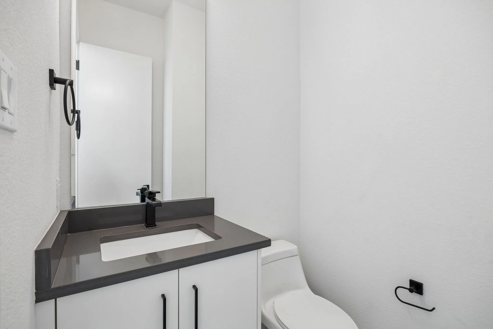 White vanity with matte black hardware, integrated rectangular sink, dark solid surface countertop, and matte black faucet