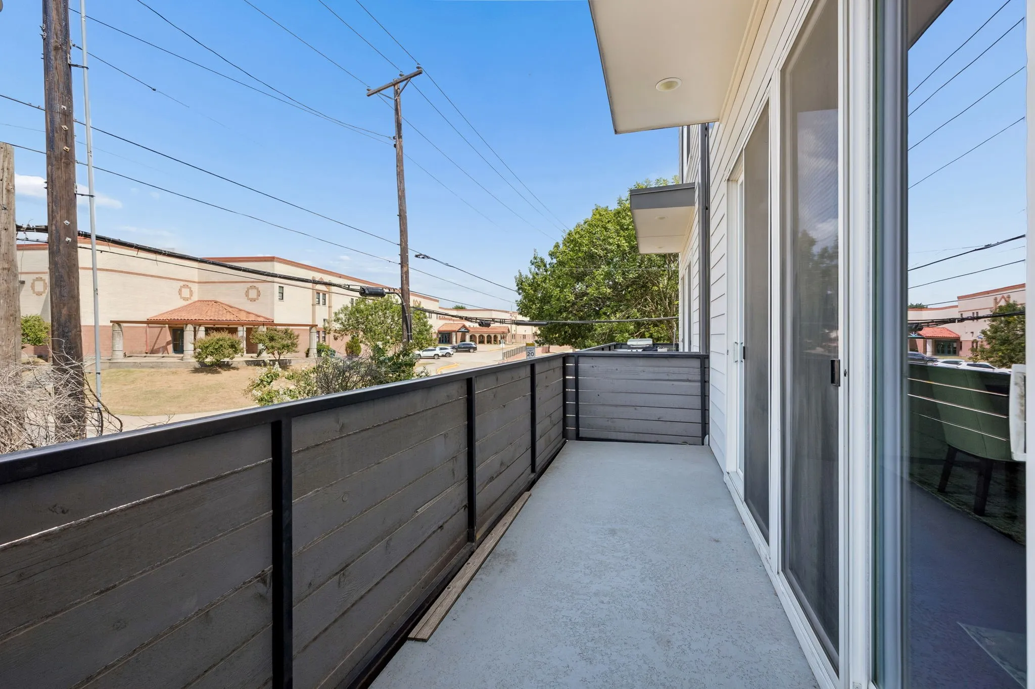 Private balcony with a concrete surface, featuring a wood-panel railing, and multiple sliding glass doors