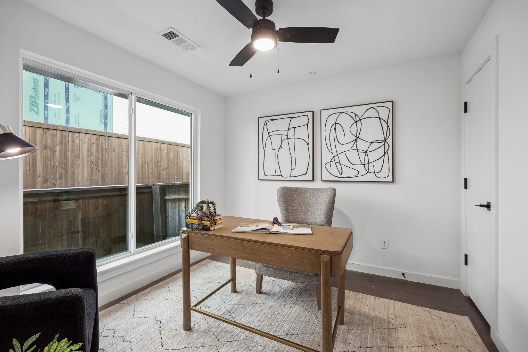 Bright interior space with a large sliding window, dark wood-finish flooring, a ceiling fan, and a white interior door with matte black hardware