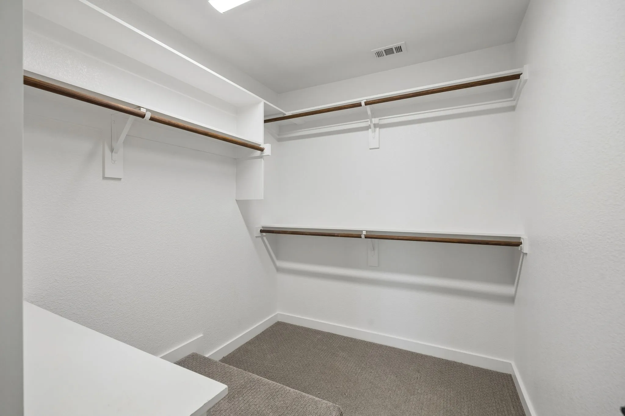 Walk-in closet with carpet flooring, white walls, built-in shelving, and multiple clothing rods