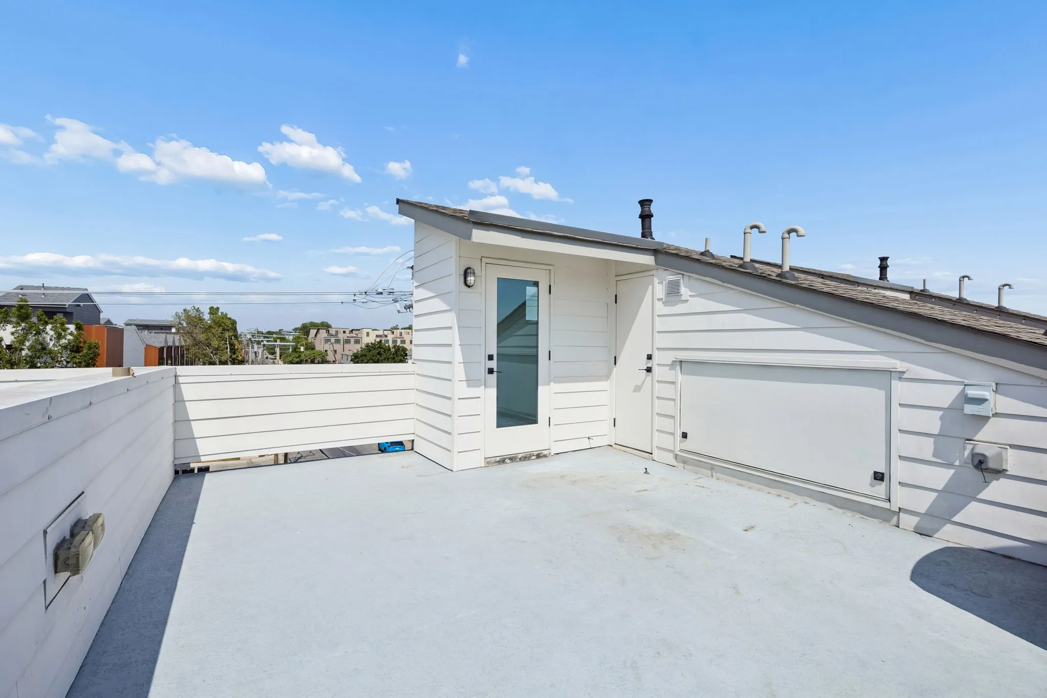 Rooftop deck with white shiplap-style walls, a glass-paneled door, and a light-colored flat roof surface