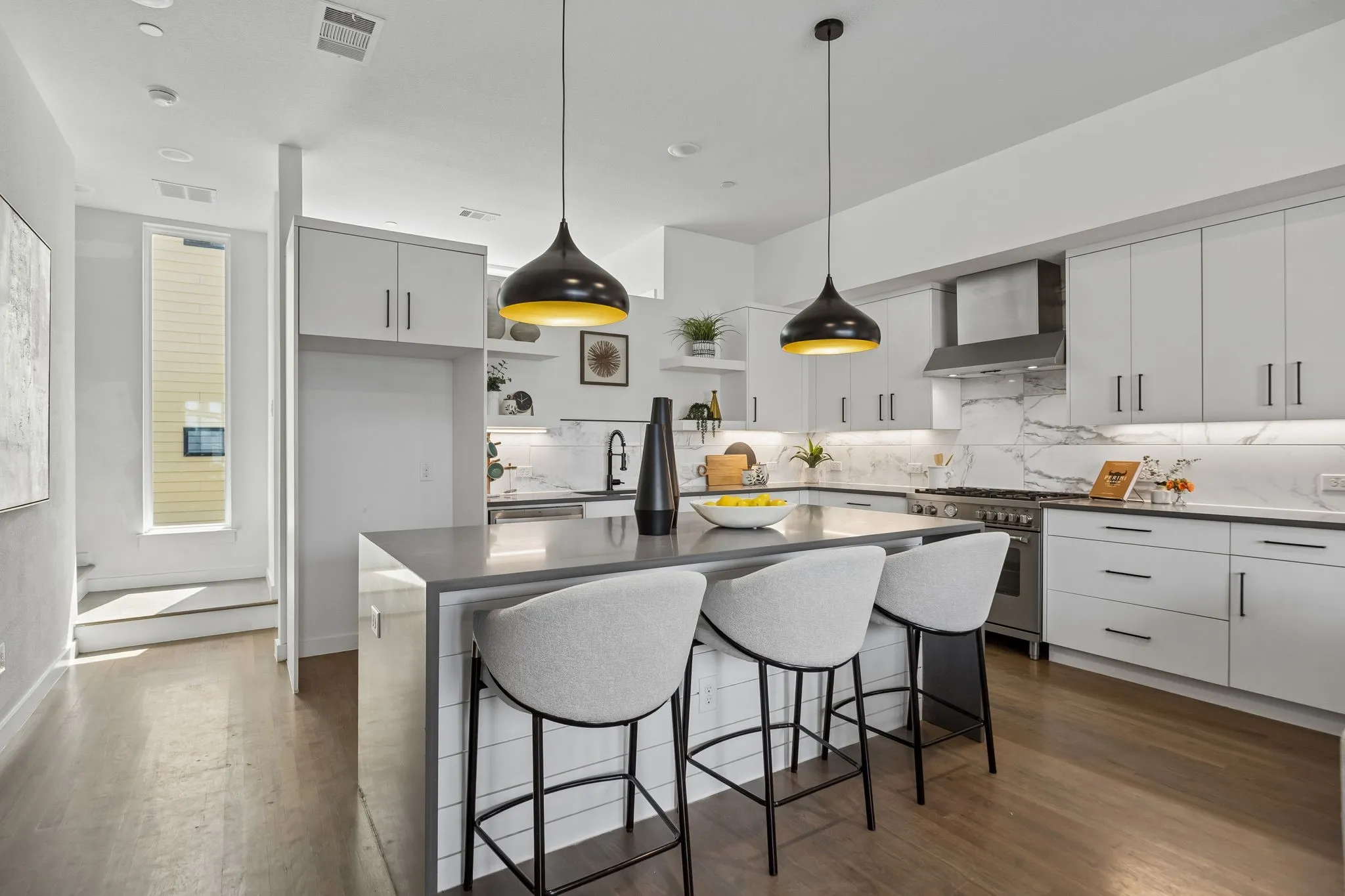 Contemporary kitchen featuring light wood-finish flooring, white cabinetry, an expansive center island, and integrated stainless steel appliances including a range and range hood