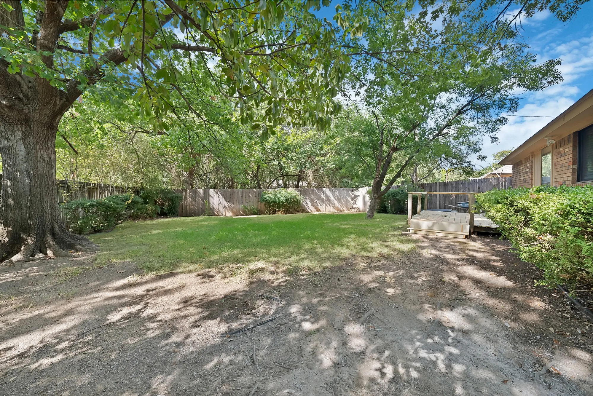 Expansive backyard featuring a manicured lawn, established trees, privacy fencing, and a wooden deck