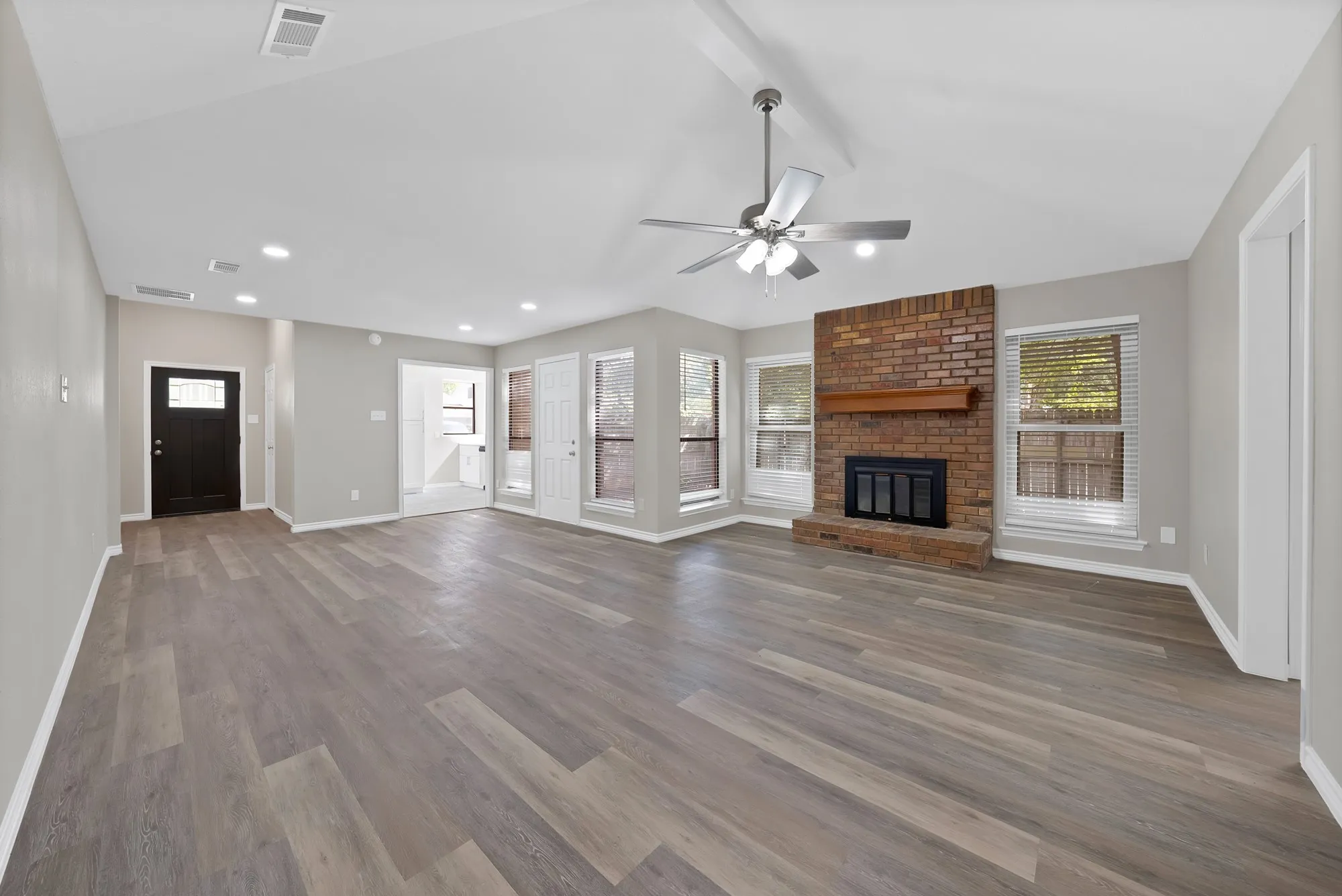 Spacious interior with vaulted ceilings, wood-finish flooring, recessed lighting, and a brick fireplace