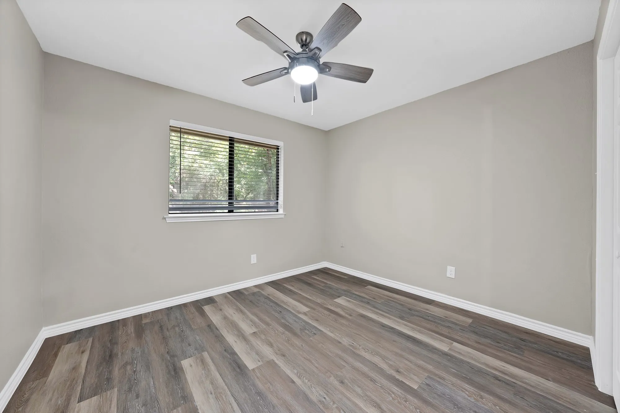 Wood-finish flooring, neutral wall tones, window with horizontal blinds, ceiling fan with integrated lighting, and white trim throughout