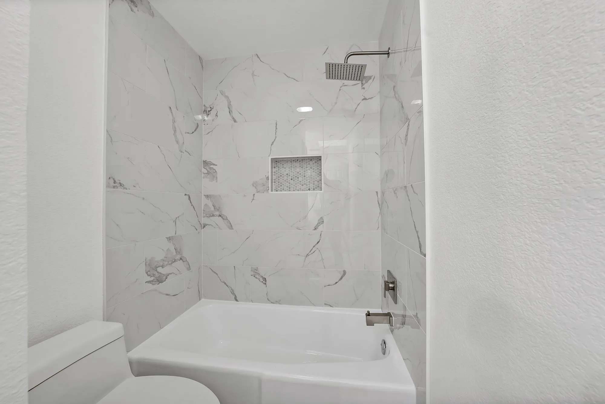 Bathtub with marble-look tile surround, mosaic tile niche, and a square rain shower head