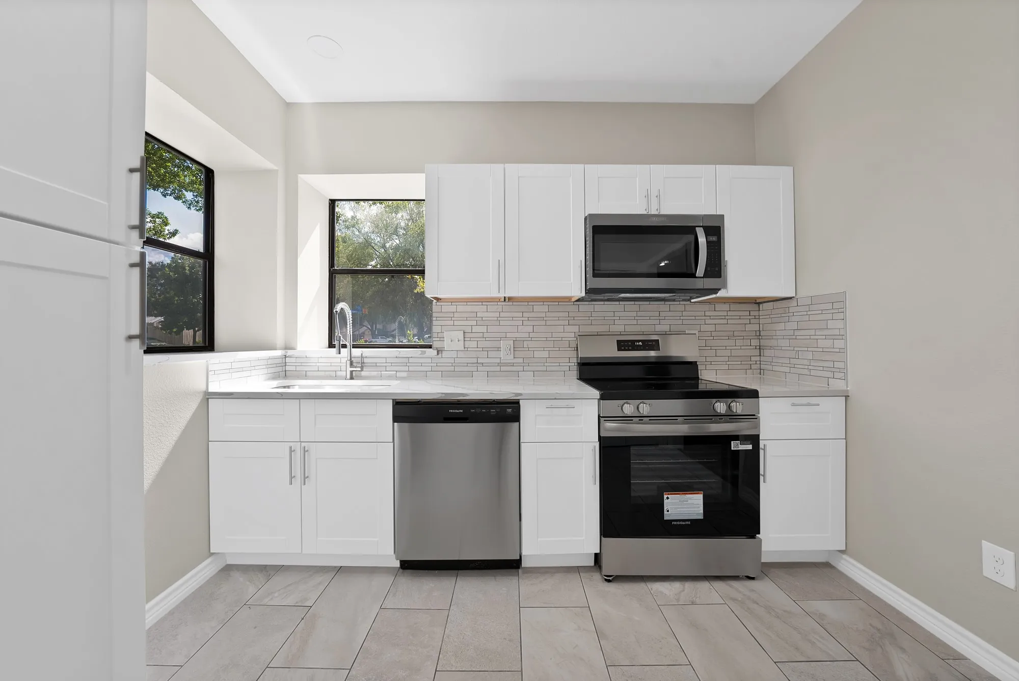 Kitchen featuring white shaker cabinetry, stainless steel appliances, a tile backsplash, light-toned countertops, and tile flooring