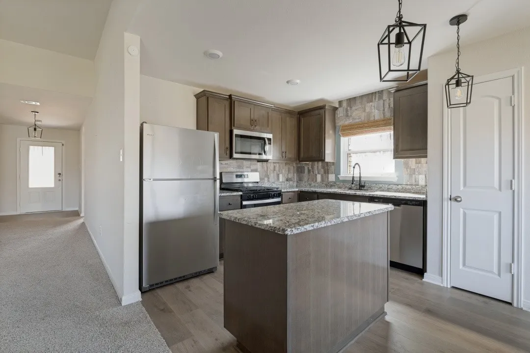 Kitchen featuring wood-finish cabinetry, a central island with a stone-finish countertop, stainless steel appliances, and pendant lighting