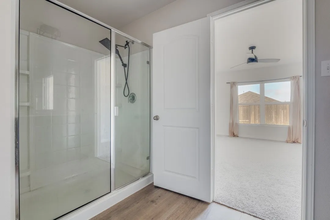 Walk-in shower with clear glass enclosure and black-finish shower fixtures, wood-finish flooring, and white paneled door