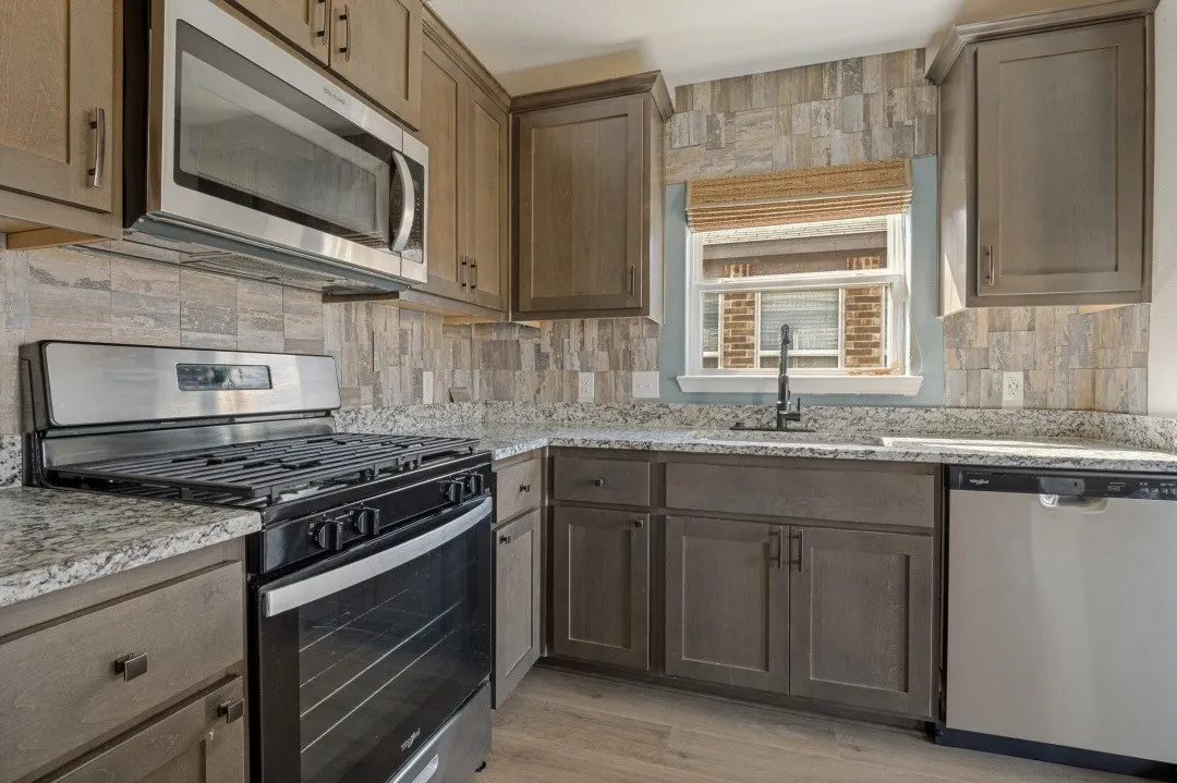 Stainless steel microwave, gas range, and dishwasher complement the light-toned cabinetry