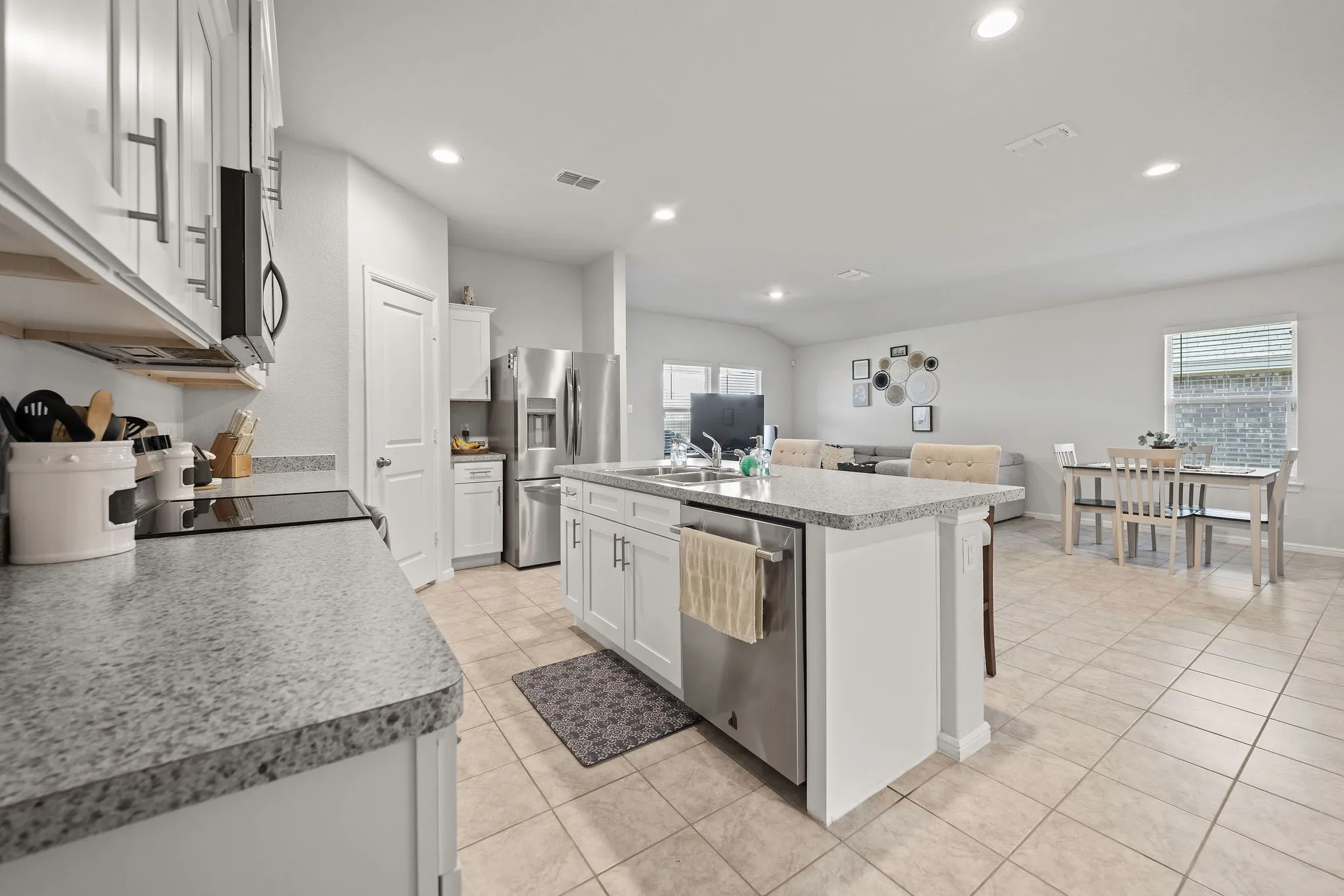 Kitchen featuring stainless steel appliances, recessed lighting, light tile patterned floors, white cabinetry, and a center island with sink