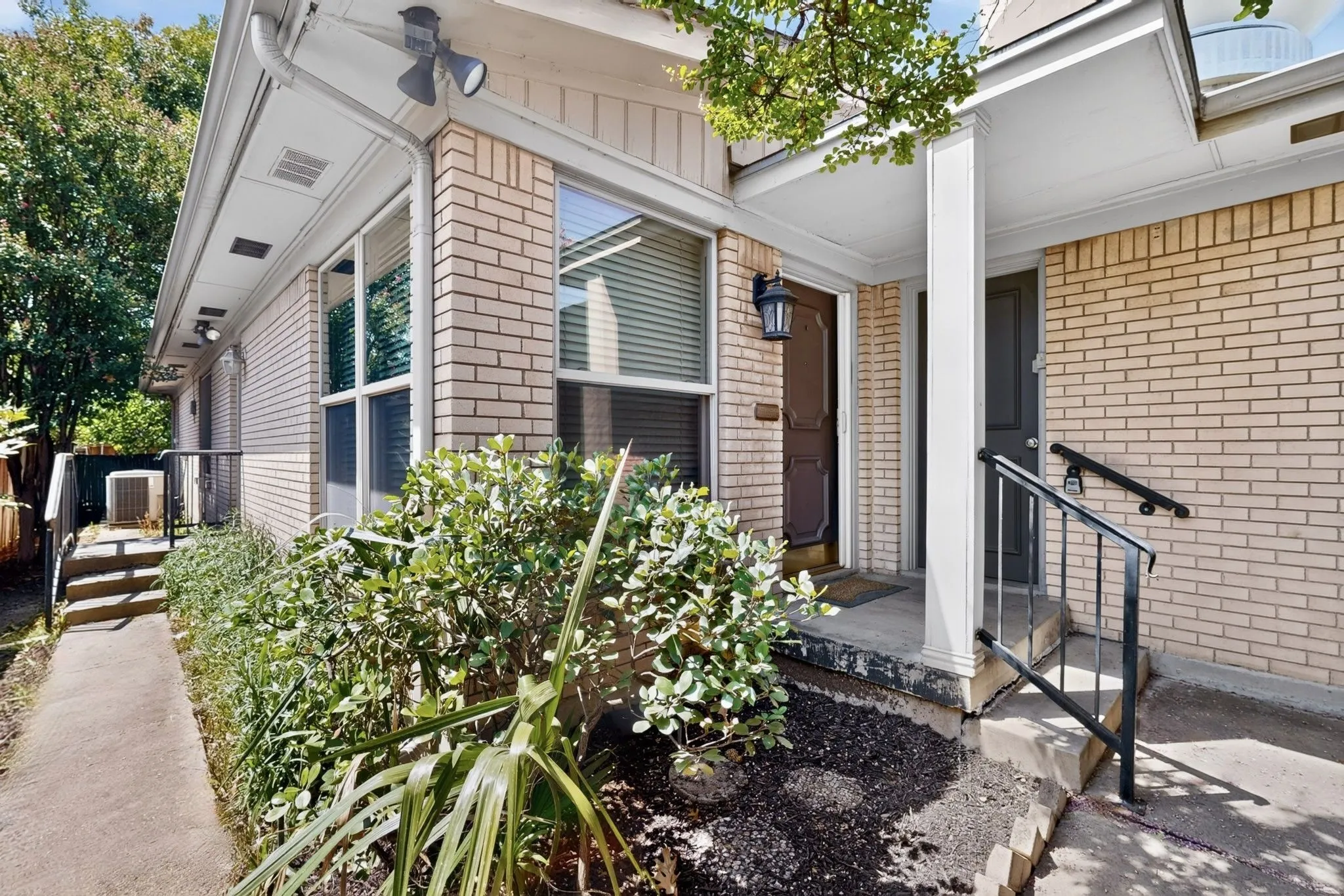 Brick exterior with a covered entry, mature landscaping, and an exterior lighting fixture