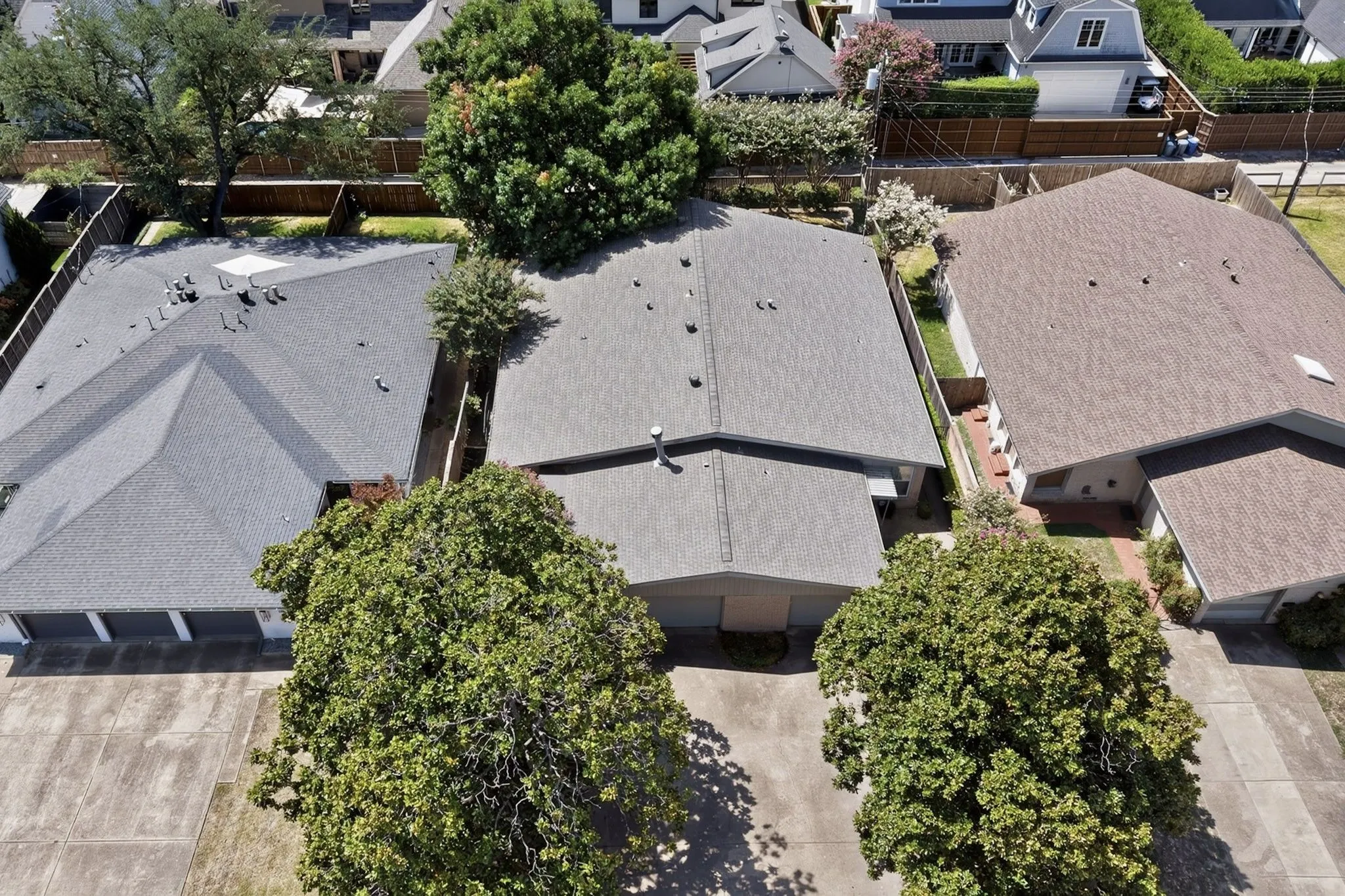 Gable roof structure with asphalt shingles, mature trees, and concrete driveway