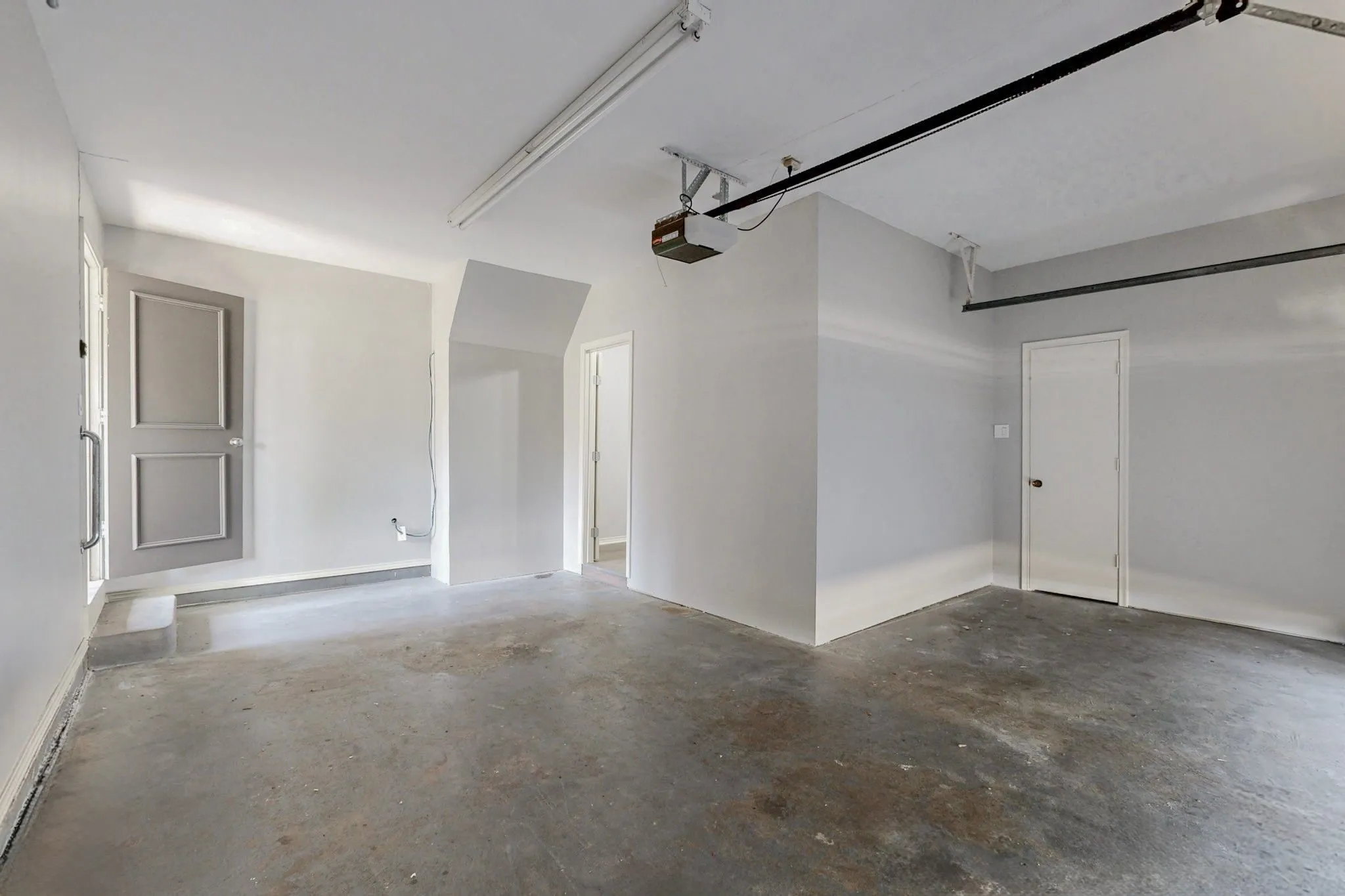 Concrete flooring, white walls, two entry doors, and overhead lighting