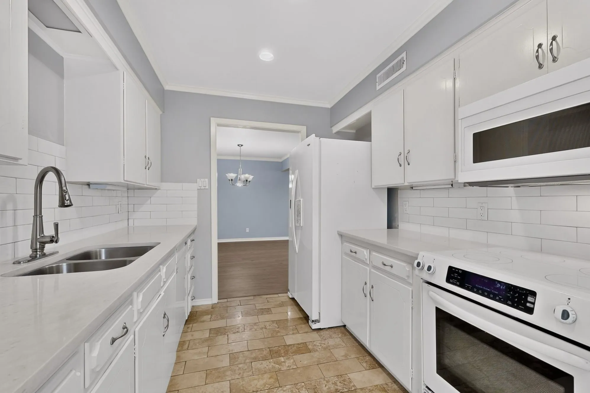White cabinetry with brushed nickel hardware, light-toned countertops, subway tile backsplash, and a stainless steel double basin sink