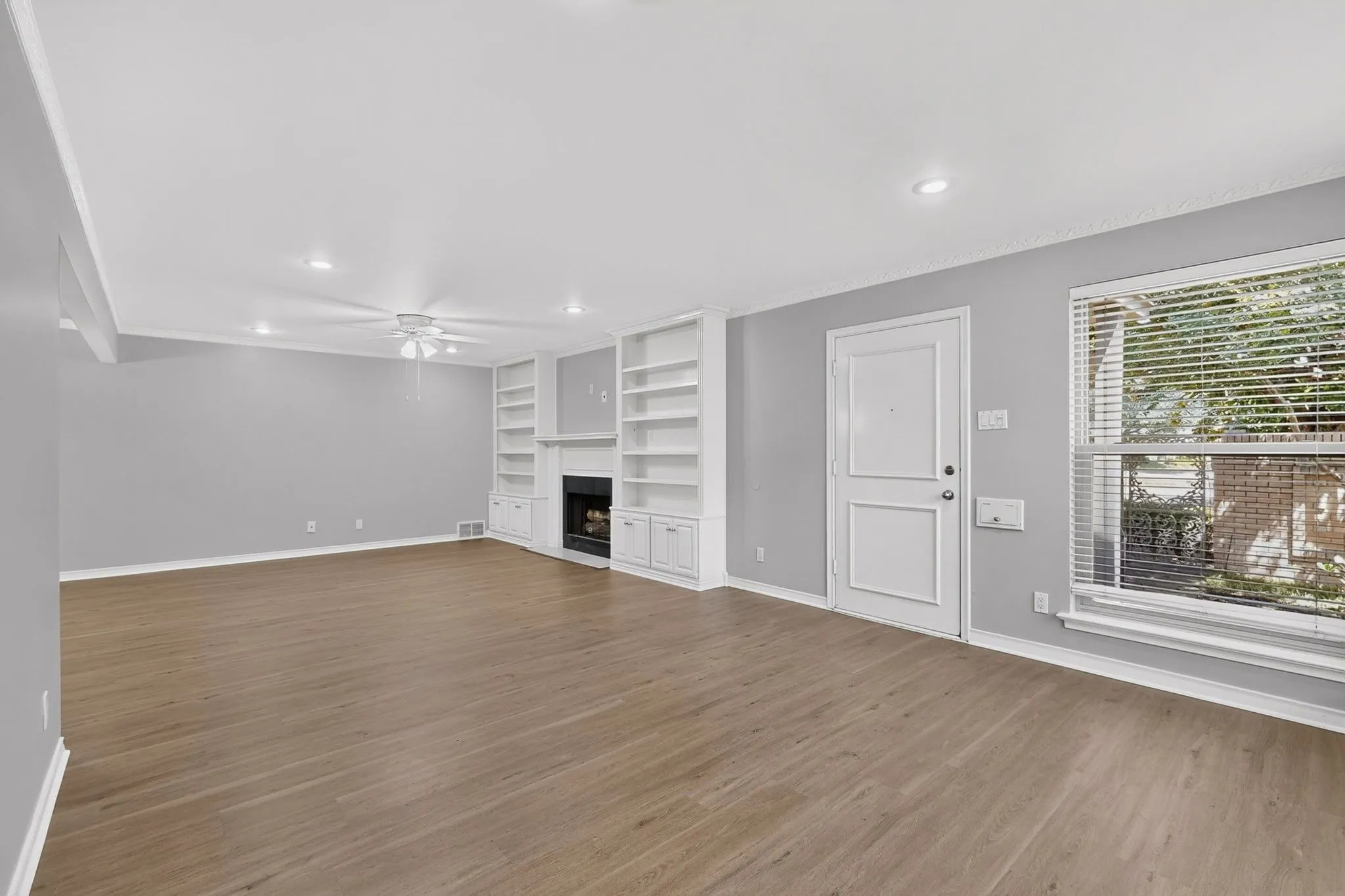 Spacious living area featuring wood-finish flooring, a white ceiling fan, recessed lighting, and a fireplace with built-in shelving