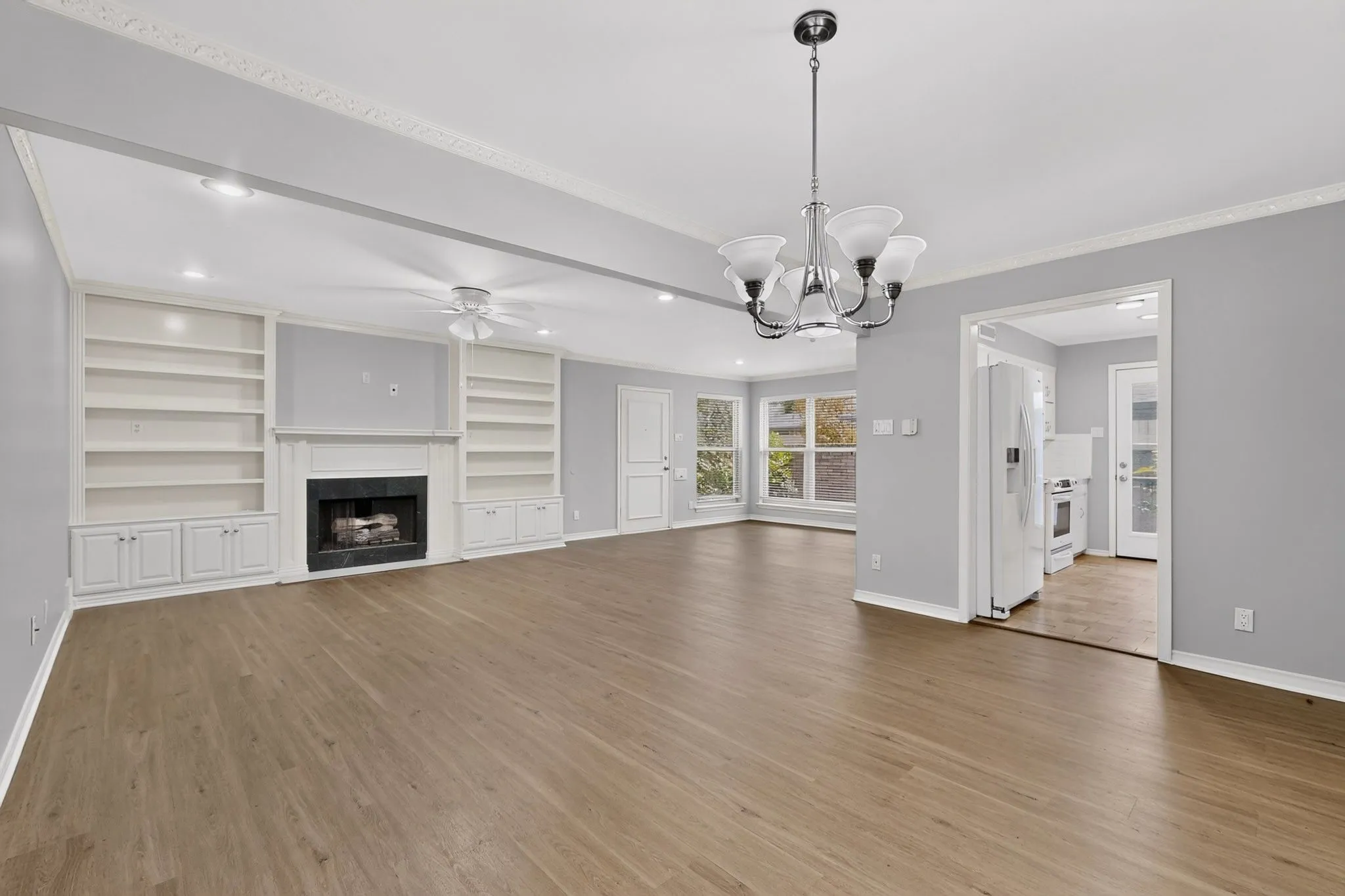Spacious room featuring wood-finish flooring, a fireplace with built-in shelving, recessed lighting, and crown molding