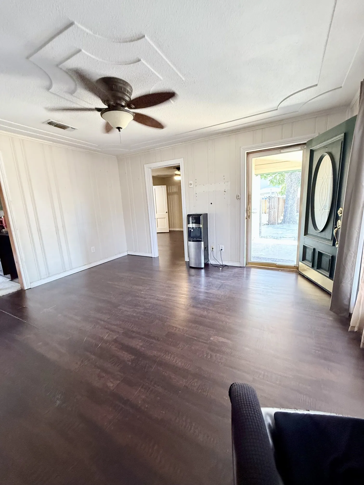 Wood-finish flooring, ceiling fan with light fixture, decorative ceiling medallion, paneled wall detailing, and an exterior door with frosted glass insert