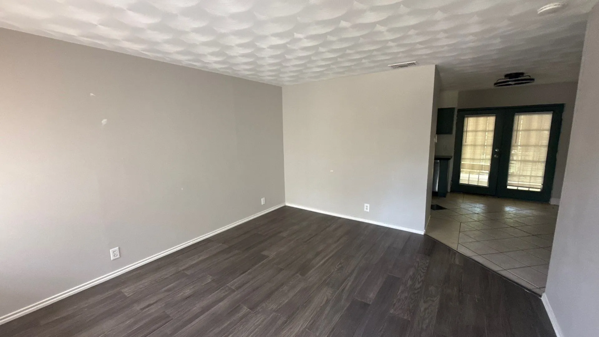 Spacious room featuring wood-finish flooring, light neutral wall tones, and a textured ceiling