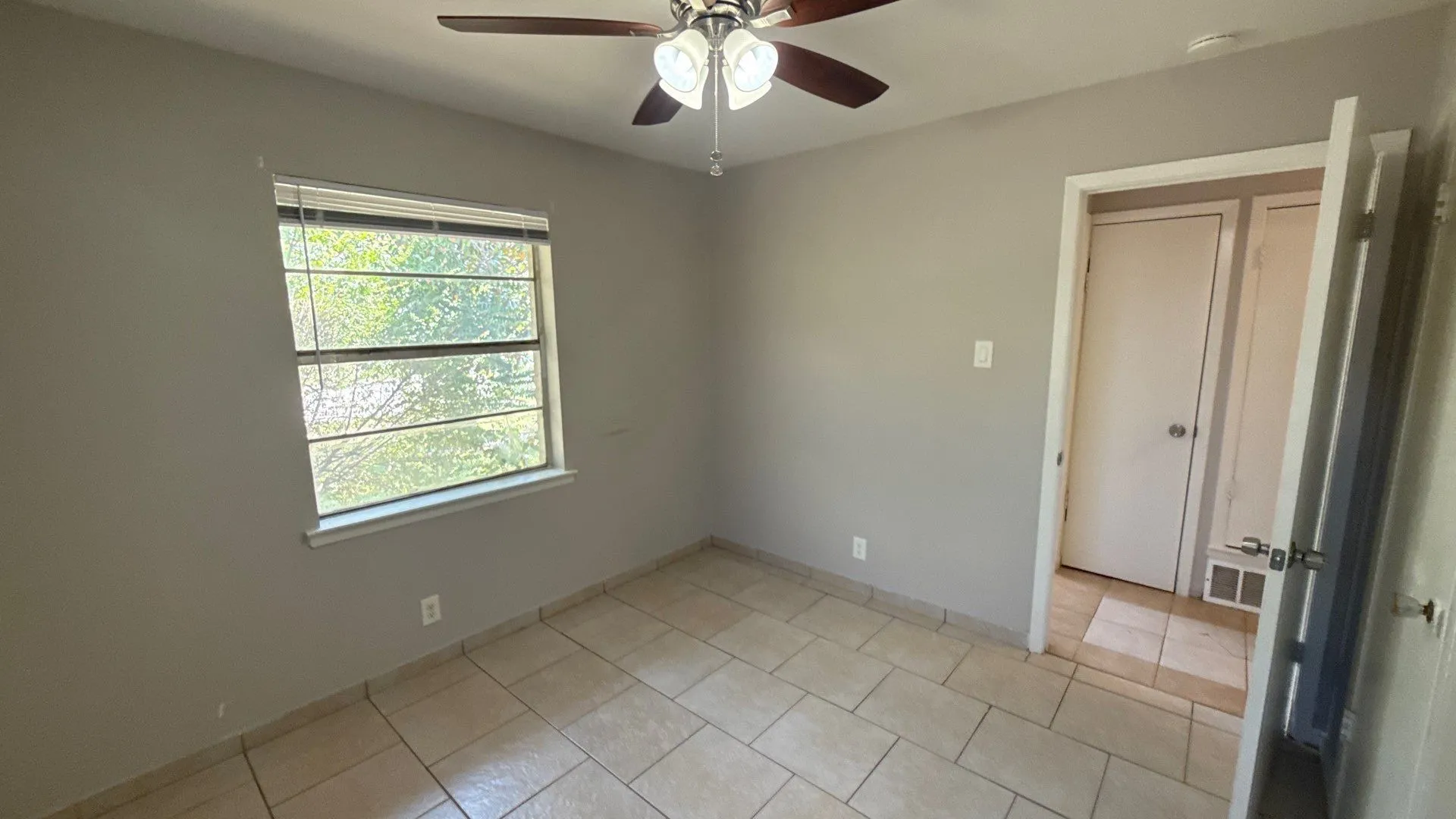 Tiled flooring, neutral wall paint, window with horizontal blinds, and a ceiling fan with integrated lighting
