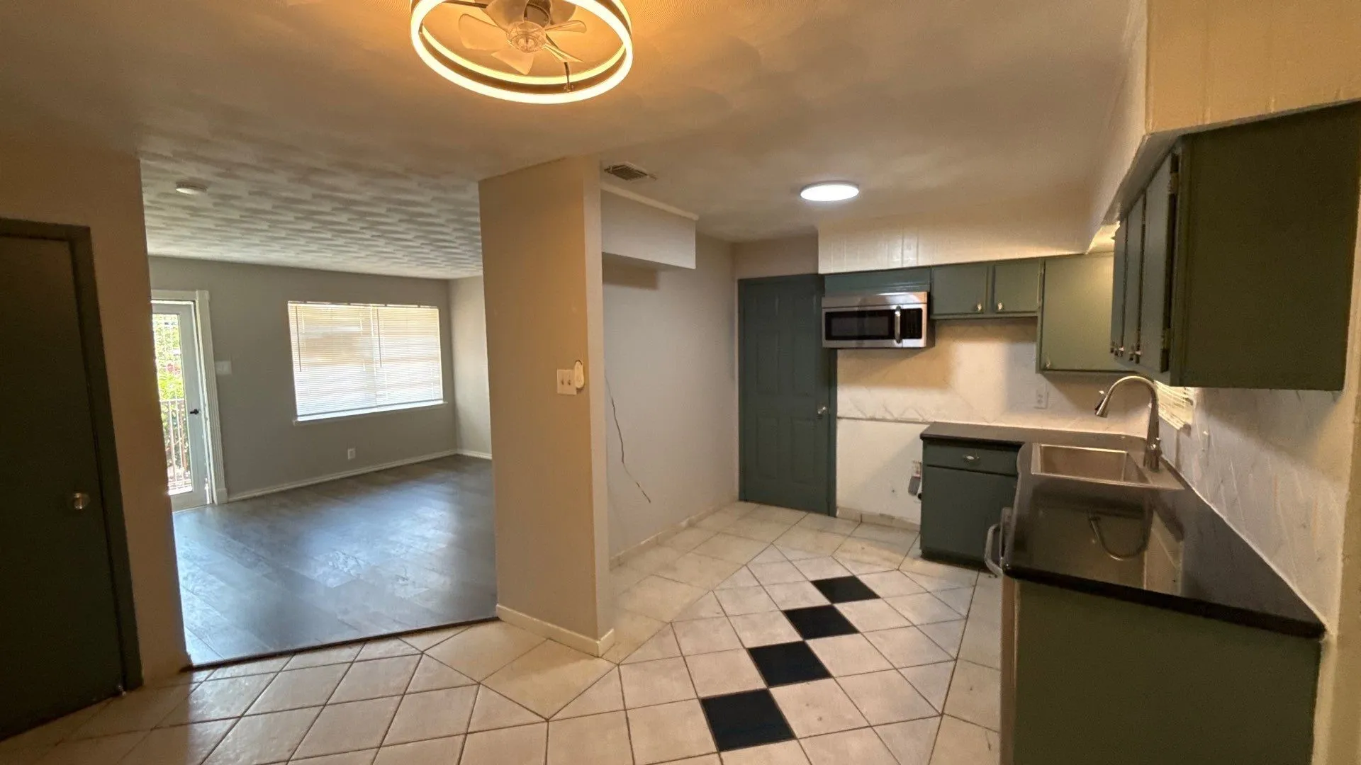 Kitchen featuring a dual-basin sink, green cabinetry, dark countertops, and tile flooring with a checkerboard pattern