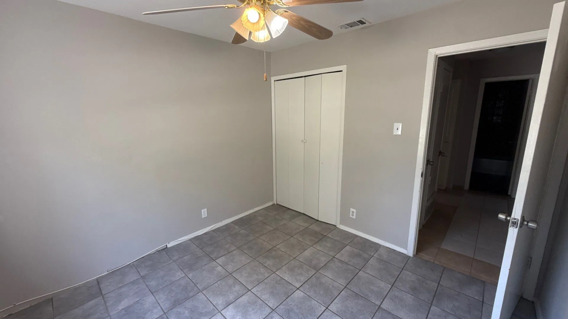 Neutral tone wall paint, tile flooring, ceiling fan with integrated lighting, bi-fold closet doors, and interior doorway