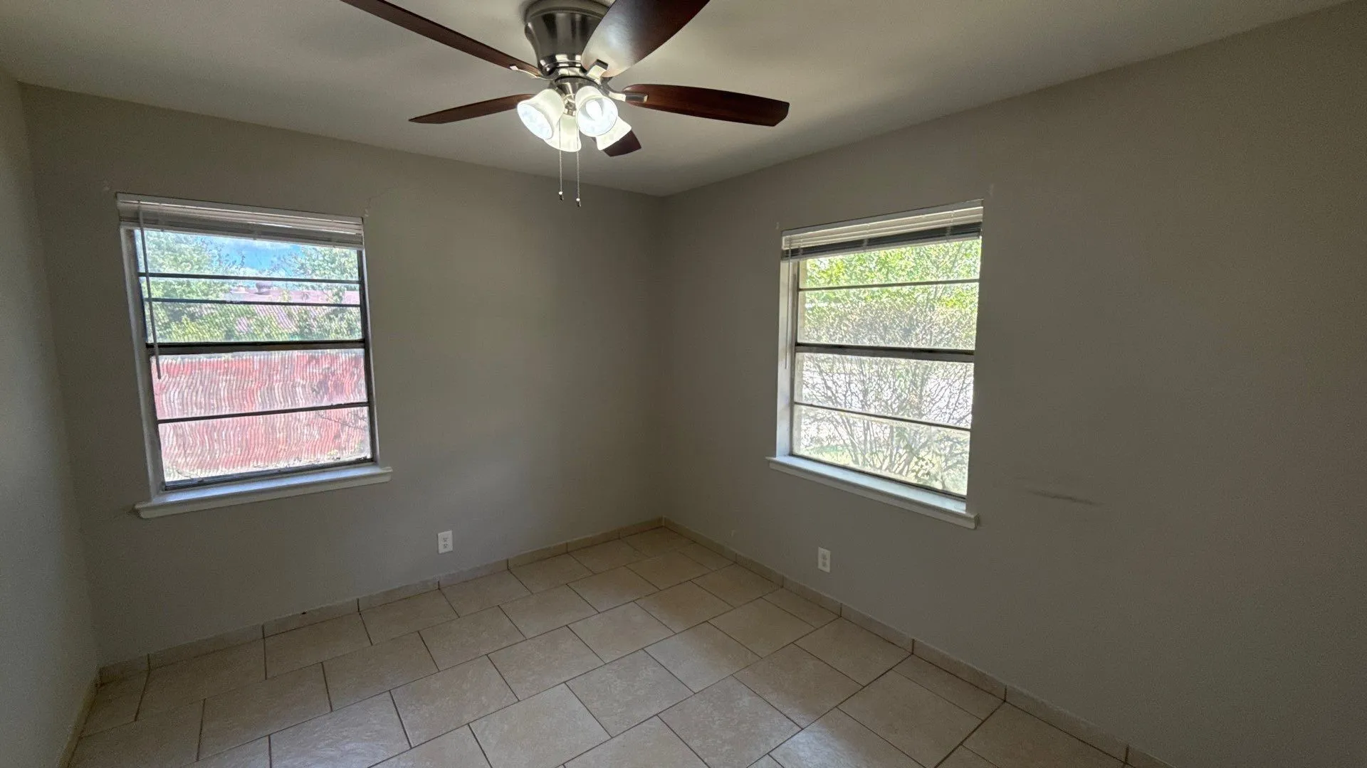 Neutral wall paint, ceiling fan with integrated lighting, two windows with blinds, and tiled flooring
