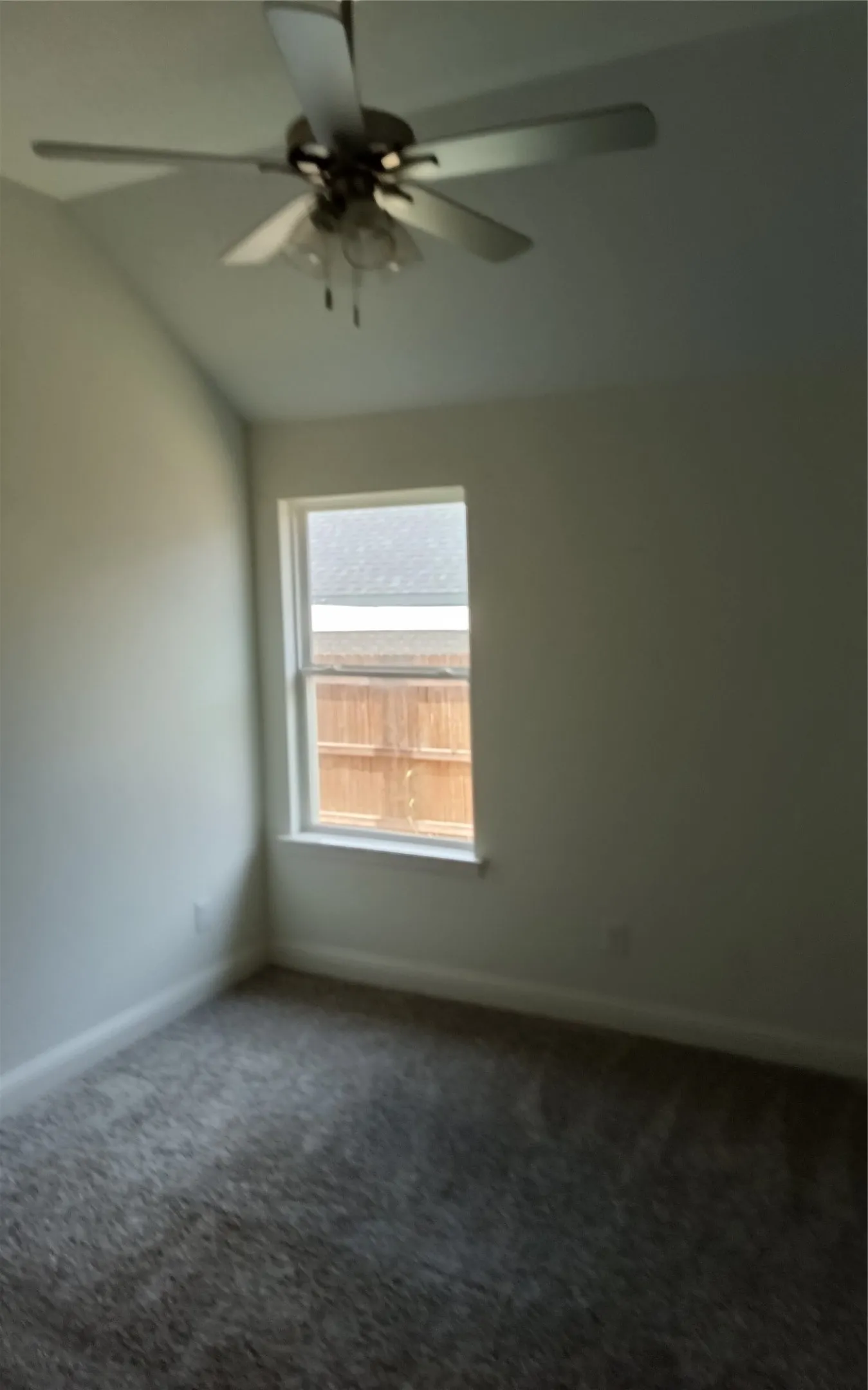 Vaulted ceiling with a ceiling fan, window with trim, and carpeted flooring