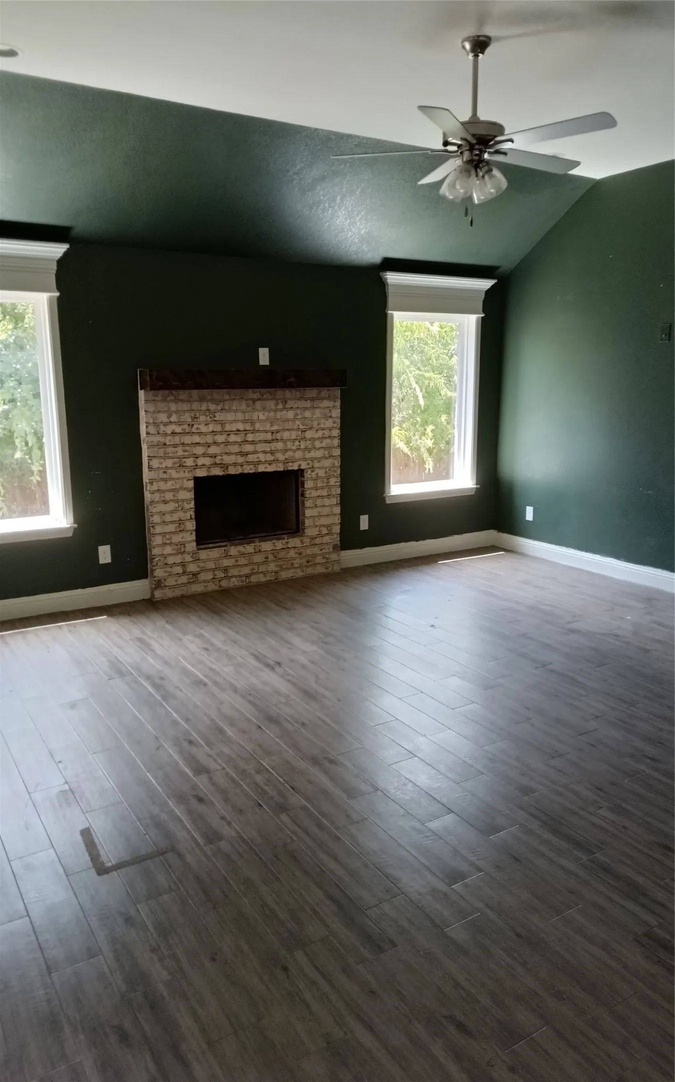 Vaulted ceiling featuring a ceiling fan, brick-front fireplace with a wood mantle, and wood-finish flooring