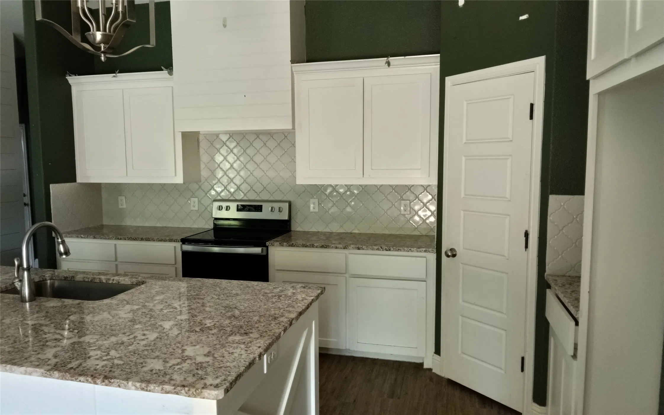 White cabinetry, tile backsplash, built-in range, wood-finish flooring, and a large kitchen island