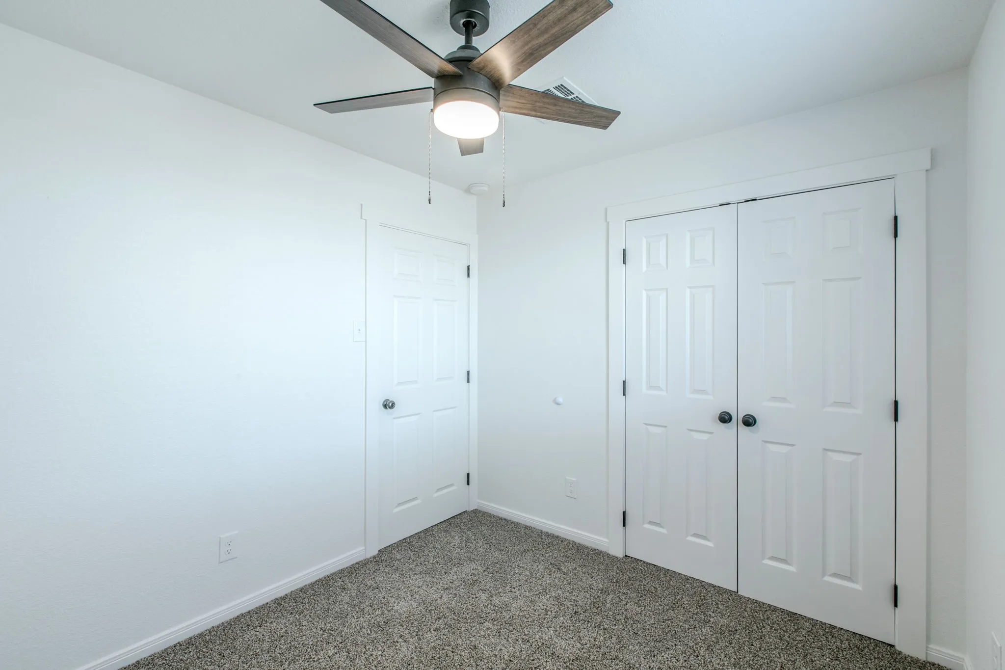 Ceiling fan with light fixture, paneled bi-fold doors, paneled interior door, and textured carpeting
