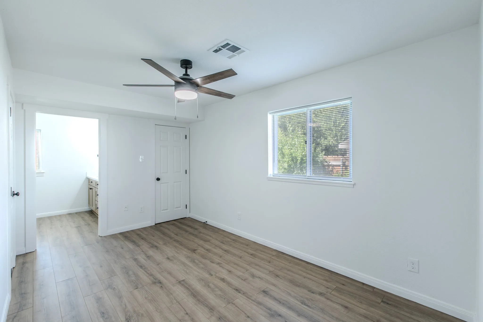 Wood-finish flooring, white walls, ceiling fan with light fixture, single window with blinds, and white interior doors