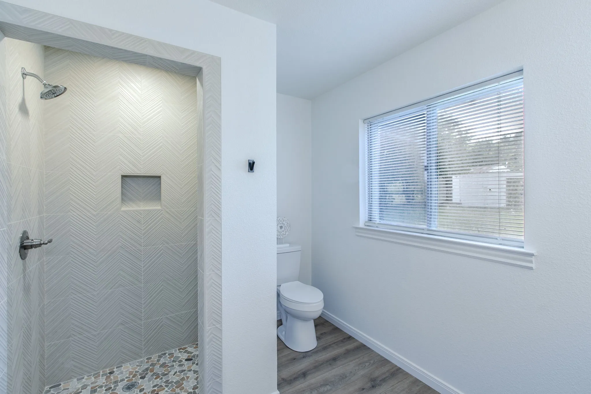 Walk-in shower with chevron-patterned tile, integrated niche, and pebble-finish flooring
