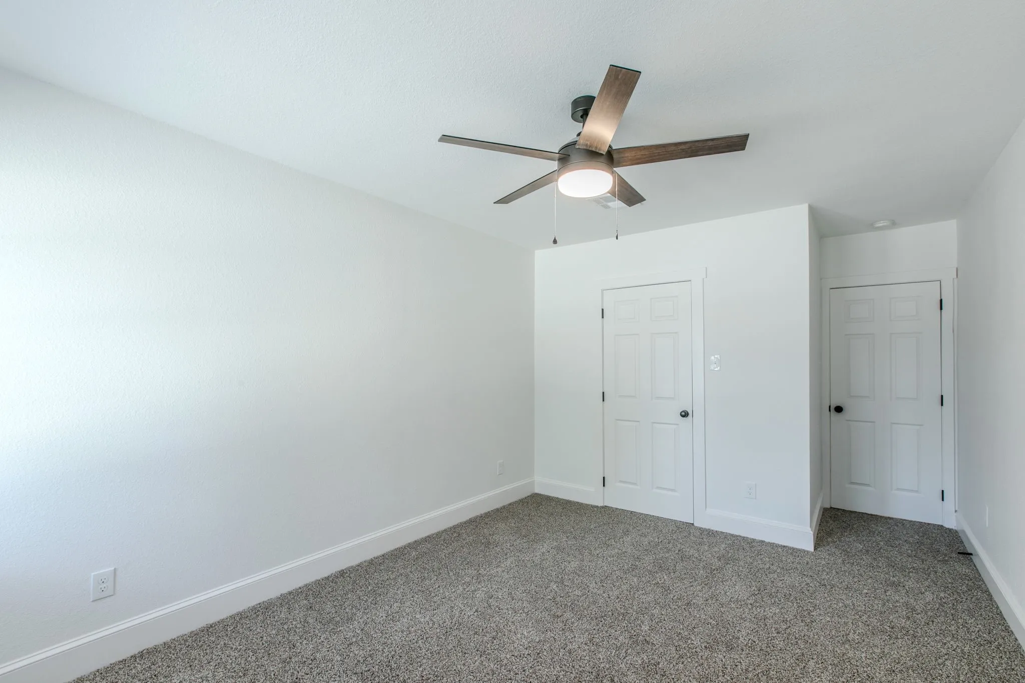 Textured walls, ceiling fan with integrated lighting, two paneled doors, and carpet flooring