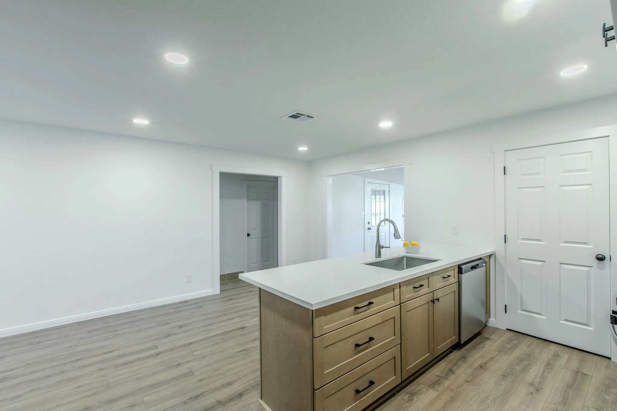 Kitchen island with light wood-finish cabinetry, stainless steel sink, and light-toned countertop