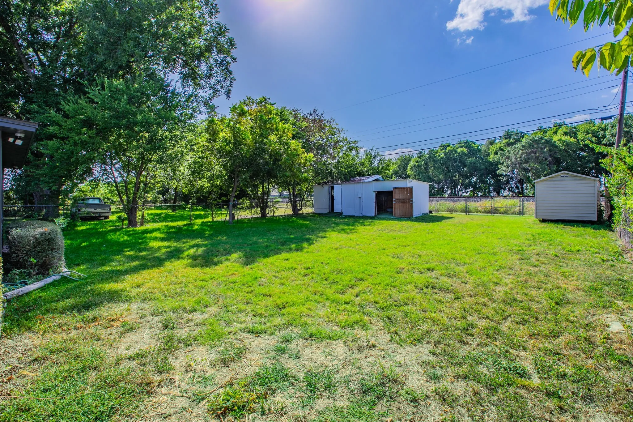 Expansive fenced yard with mature trees, two storage sheds, and a chain-link perimeter