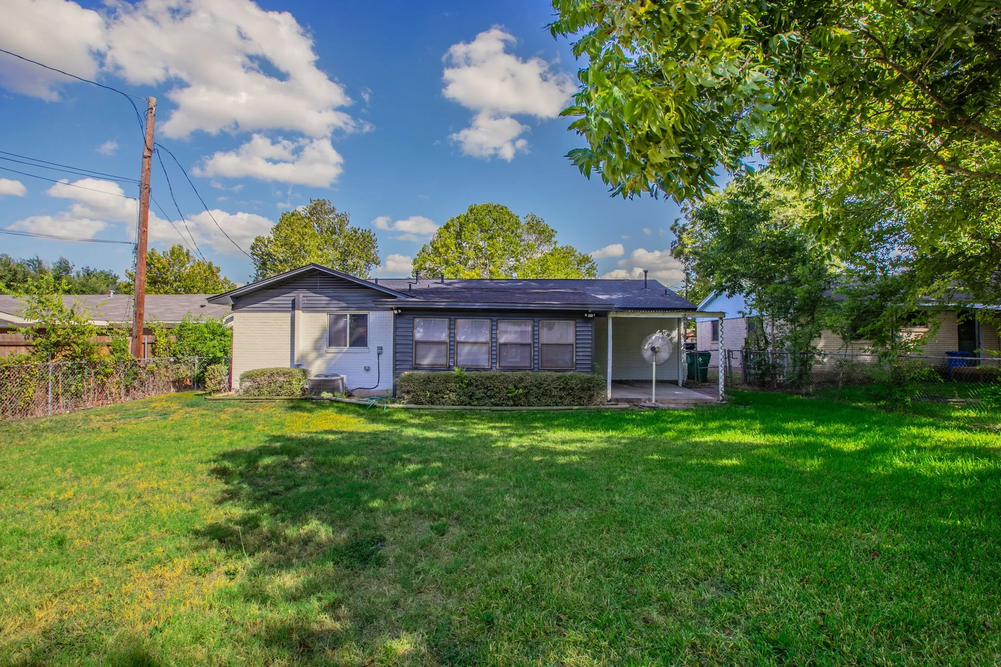 Expansive rear yard with a covered patio, mature landscaping, and a low-maintenance chain link fence