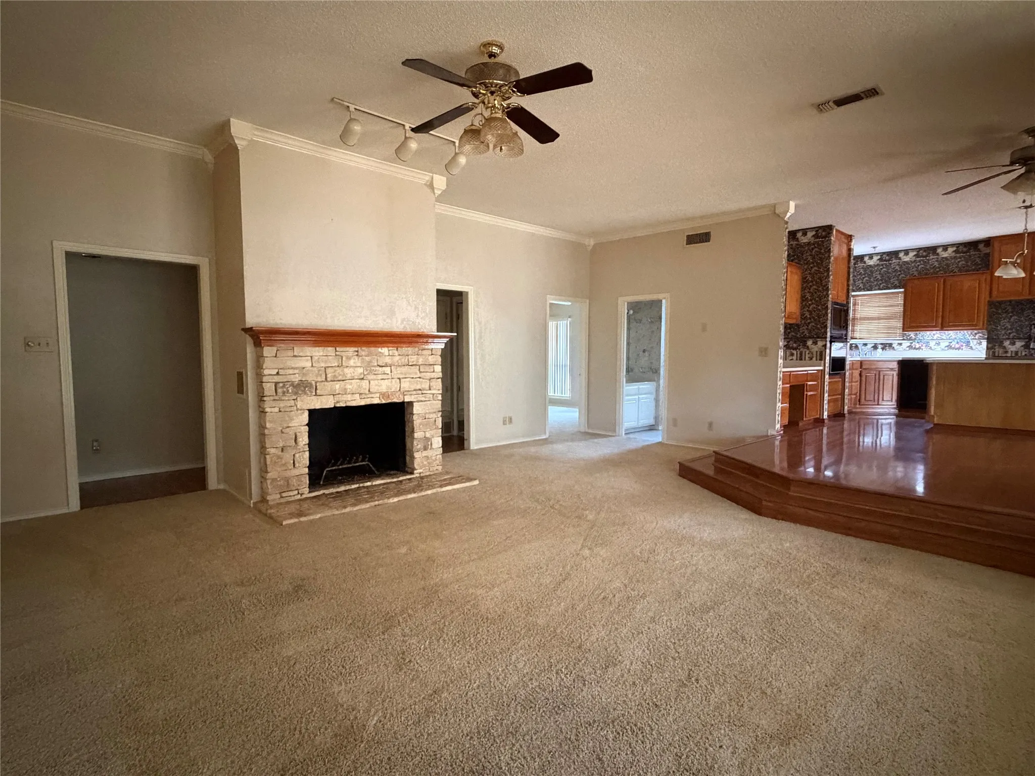 Spacious living area featuring neutral carpeting, a brick fireplace with dark surround, ceiling fan with integrated lighting, and abundant natural light from multiple glass-panel doors and windows