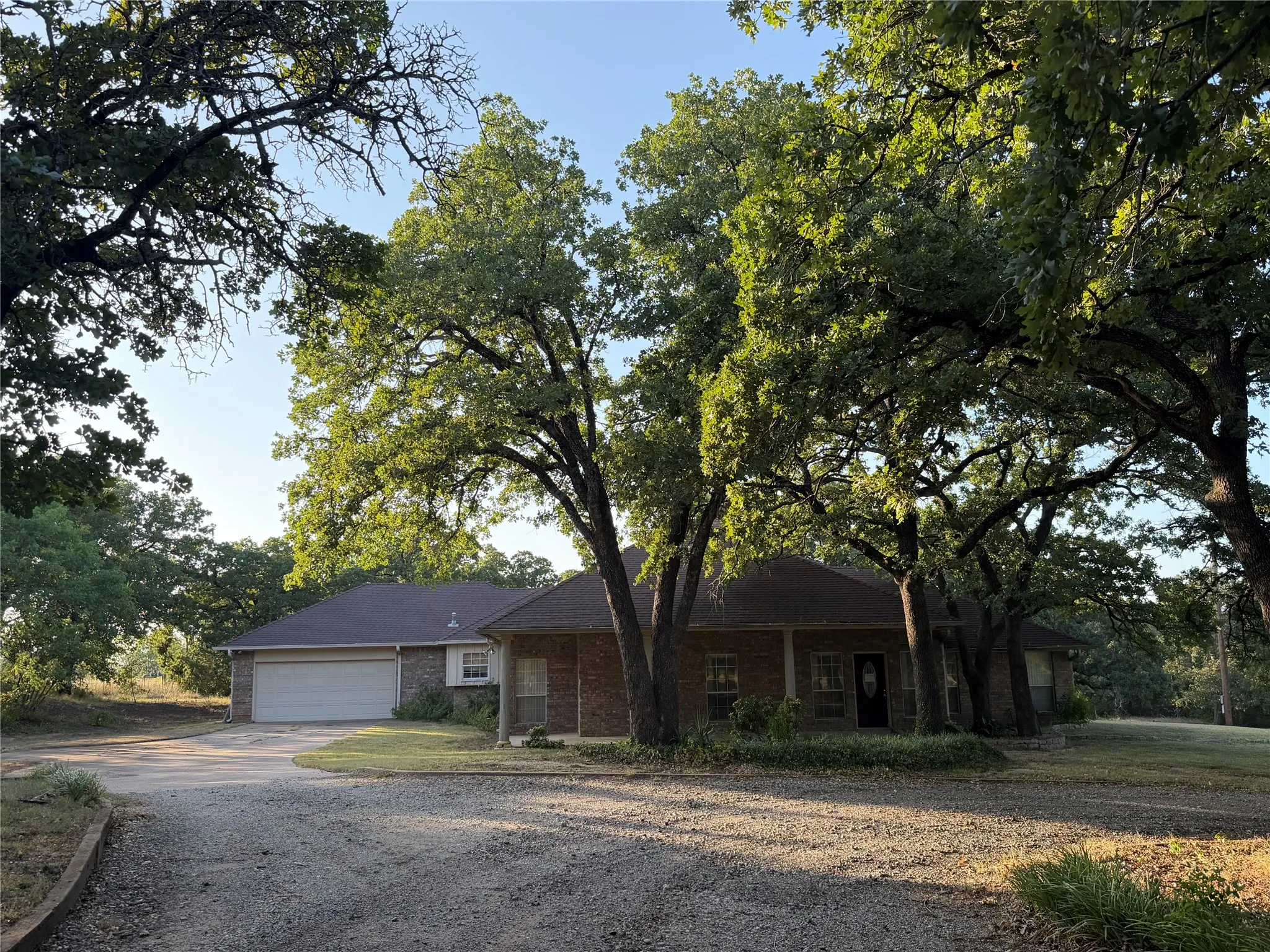 Brick exterior residence featuring a covered front porch, attached garage with a white door, and a gravel driveway