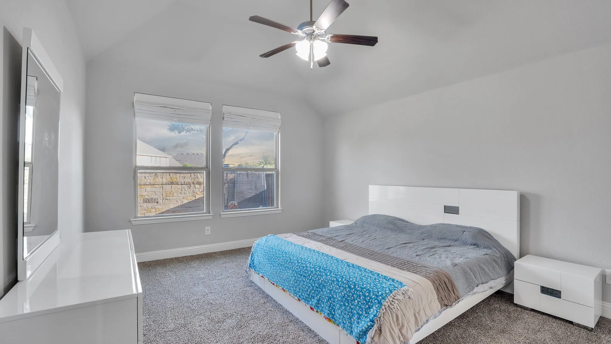 Vaulted ceiling with a ceiling fan, carpeted flooring, and two windows with blinds