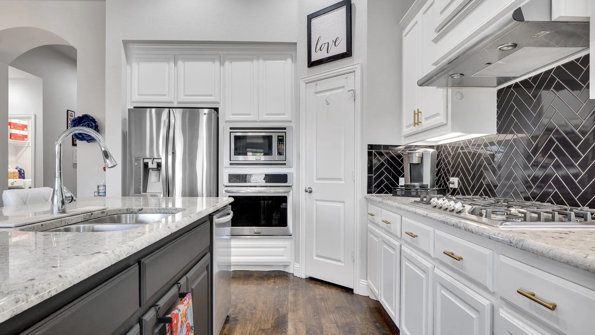 Gourmet kitchen with stainless steel appliances, granite countertops, a herringbone tile backsplash, an integrated gas cooktop, and contrasting white and dark cabinetry