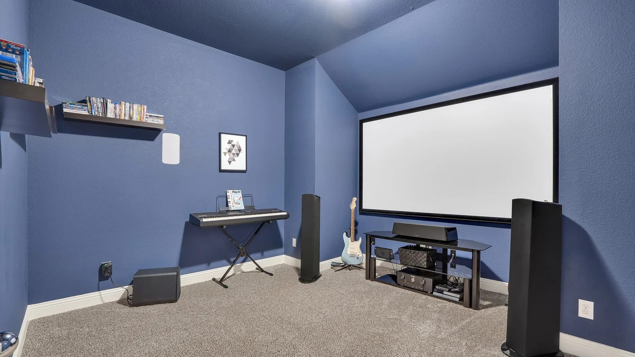 Media room featuring a large projection screen, built-in shelving, sloped ceiling, and carpeted flooring