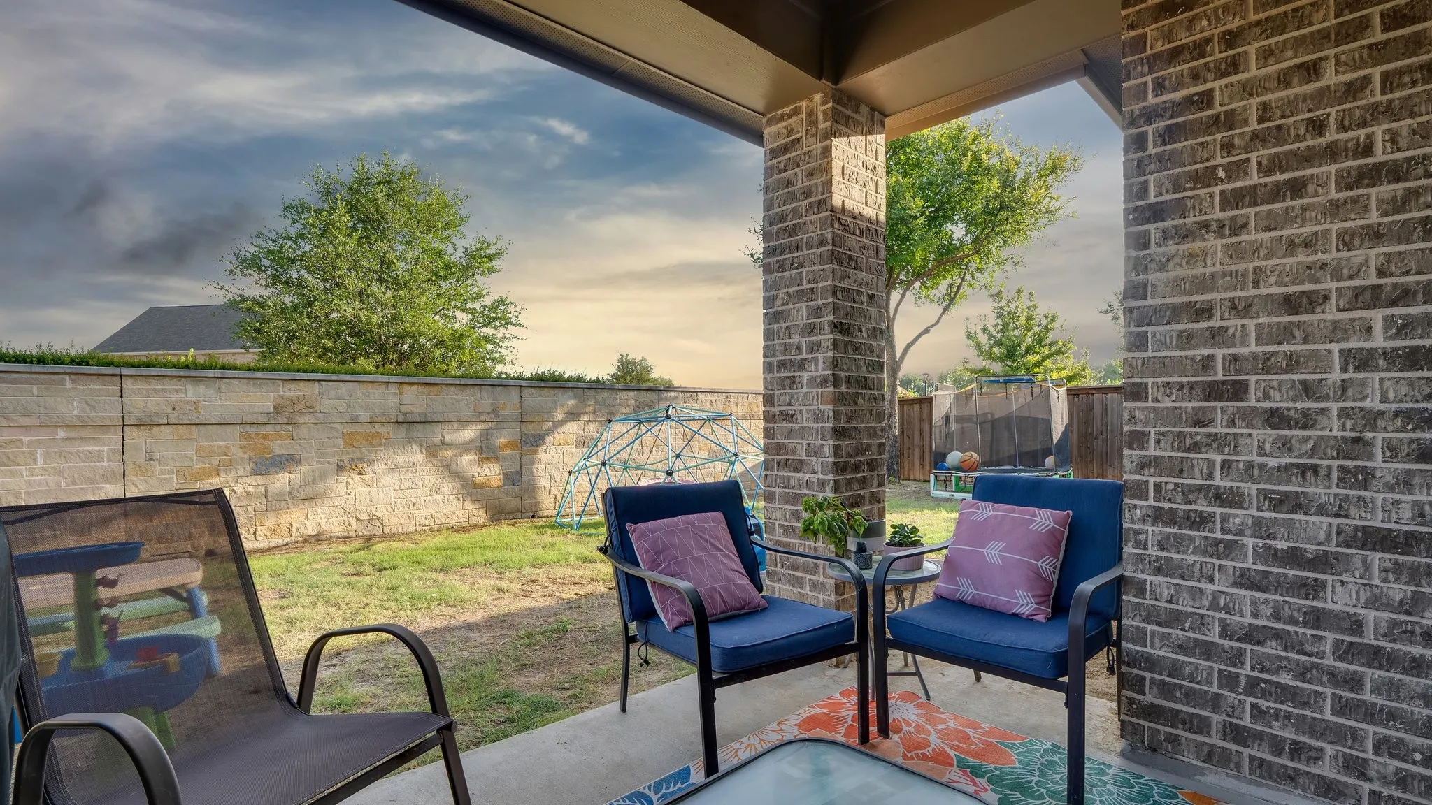Covered patio featuring brick columns, concrete flooring, and a stone retaining wall