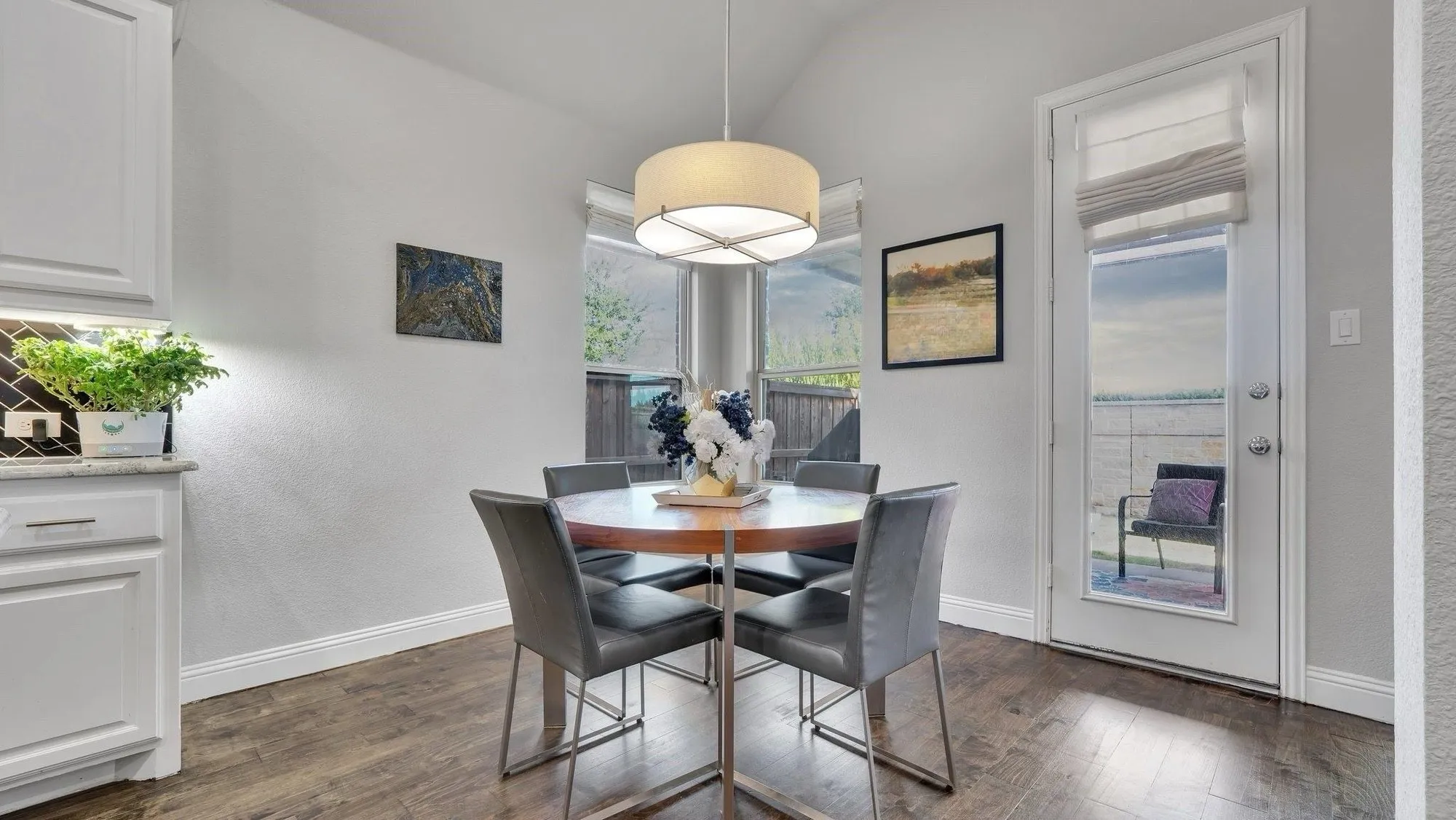 Vaulted ceiling with drum pendant lighting, wood-finish flooring, white cabinetry with dark backsplash, and a glass-paneled door