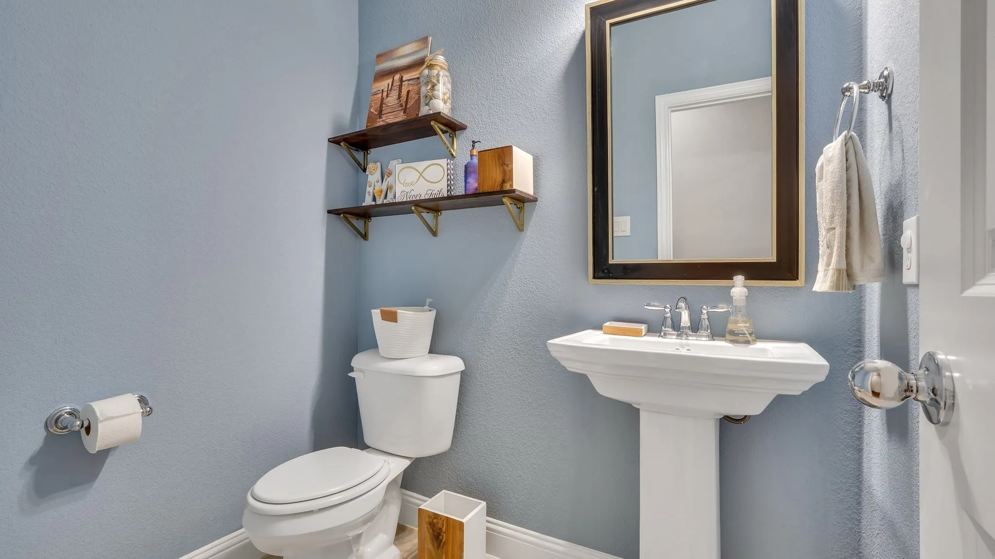 Pedestal sink with chrome fixtures, framed mirror, and floating corner shelving