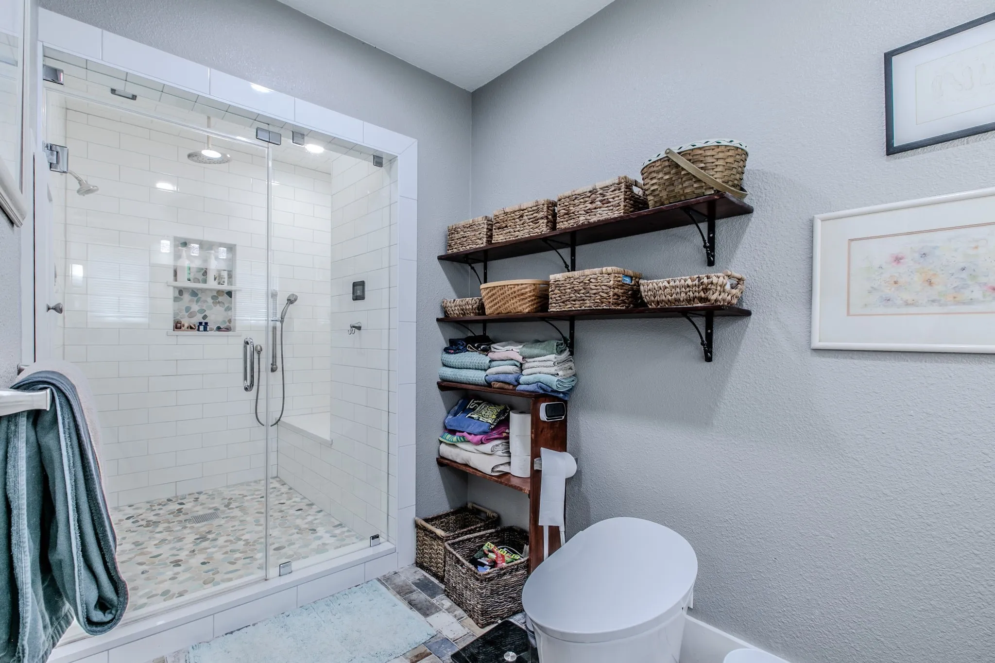 Glass-enclosed shower with subway tile, built-in shelving, and pebble-finish floor
