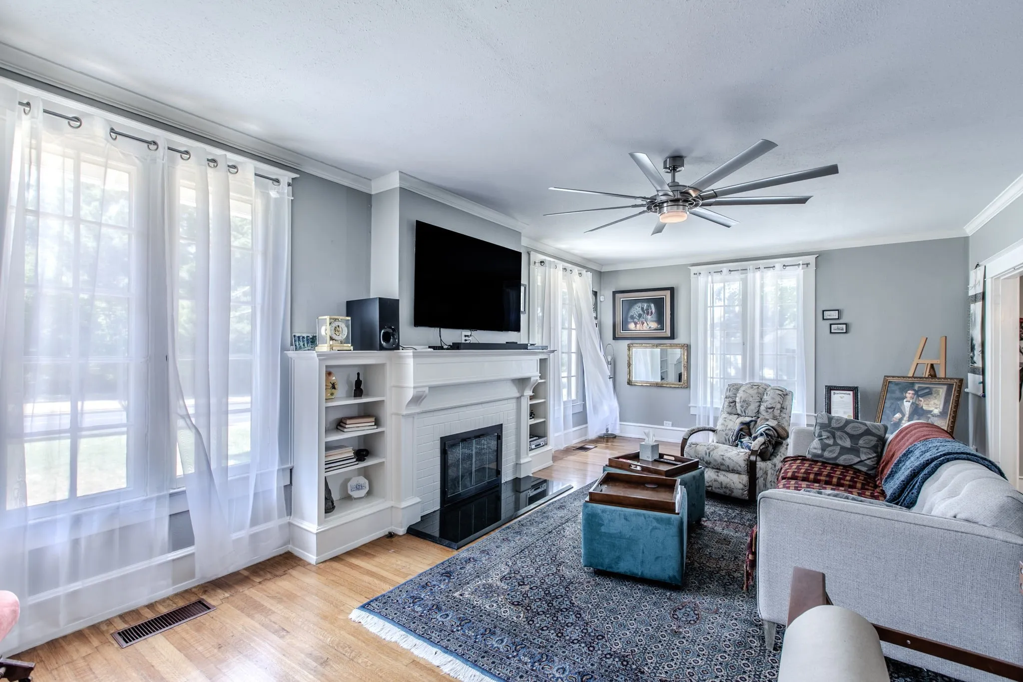 Hardwood flooring throughout, featuring a fireplace with built-in shelving, crown molding, and a multi-blade ceiling fan